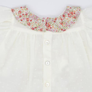 Blusa blanca con bolsillos y volante en el cuello de flores rojas, volantes en las sisas. Lazo en el bolsillo.