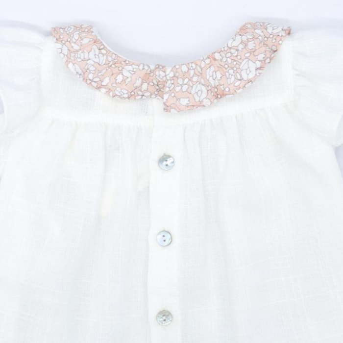 Blusa blanca con bolsillos y volante en el cuello de flores rosas, volantes en las sisas. Lazo en el bolsillo.