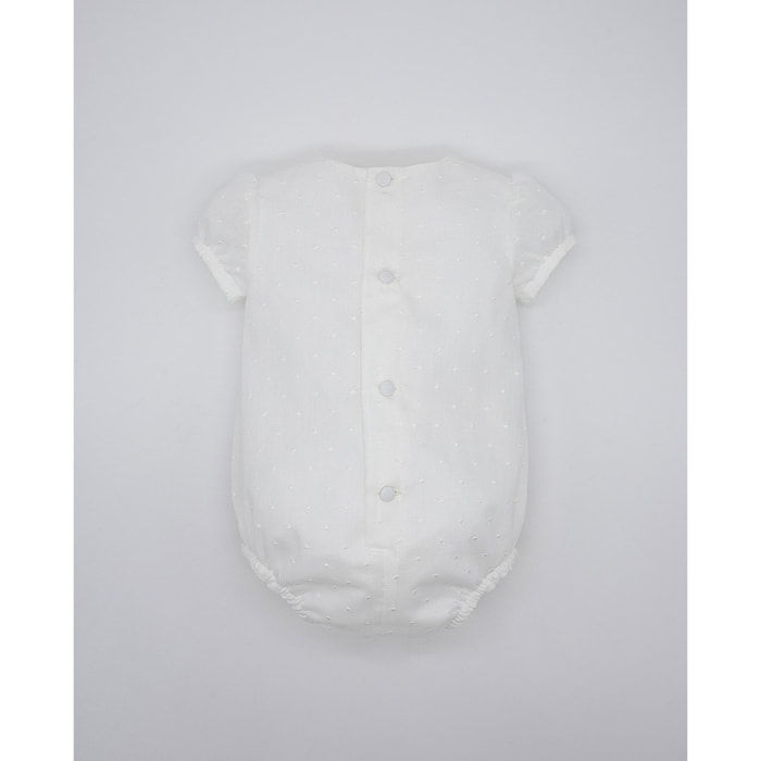 Pelele de muselina bordada blanca, de manga corta. Con puntilla y fruncido en el pecho.