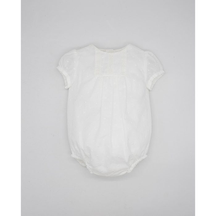 Pelele de muselina bordada blanca, de manga corta. Con puntilla y fruncido en el pecho.