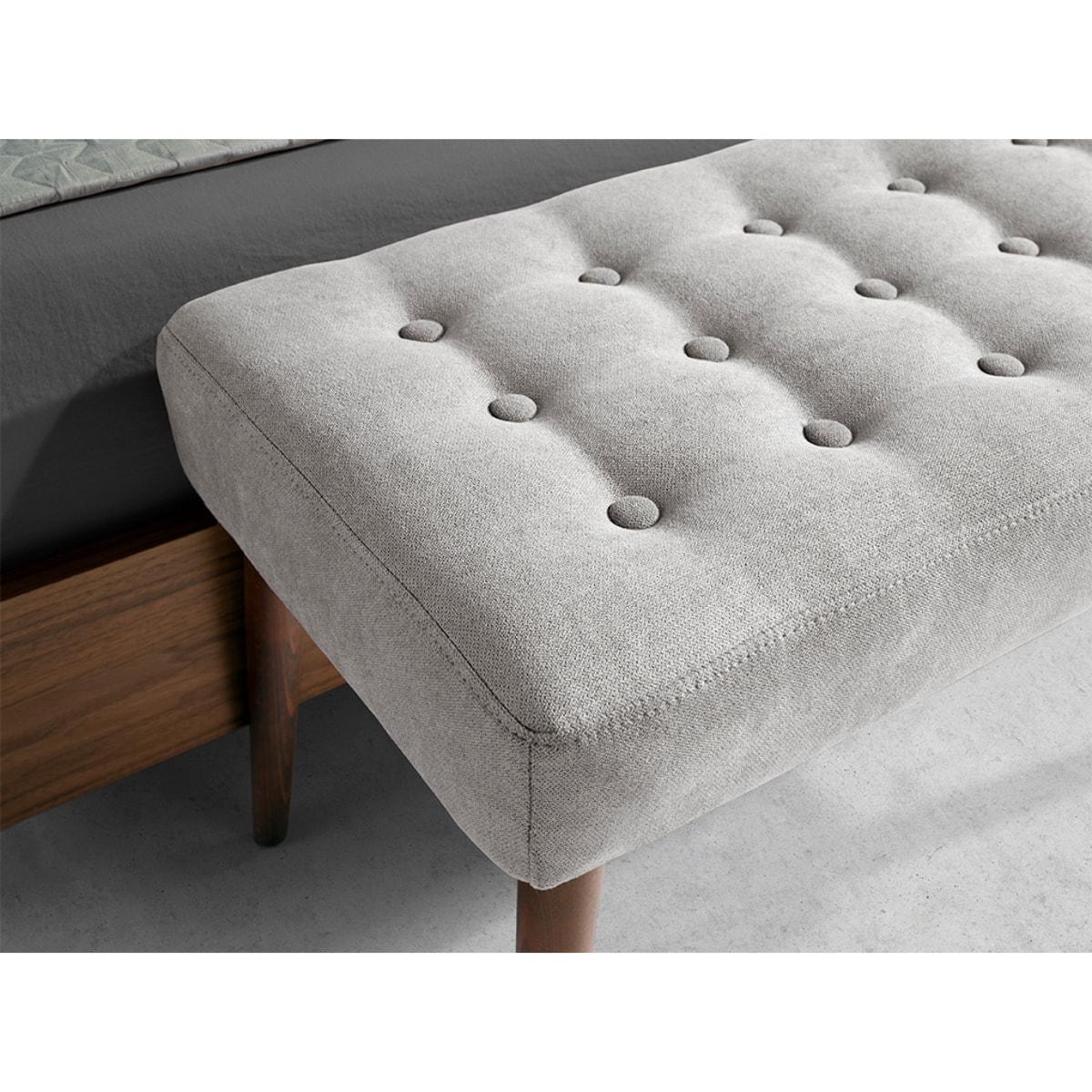 Banqueta tapizada en tela gris oscuro con estructura de patas de madera en nogal 100x40x45cm