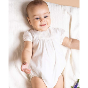 Pelele de muselina bordada blanca, de manga corta. Con puntilla y fruncido en el pecho.