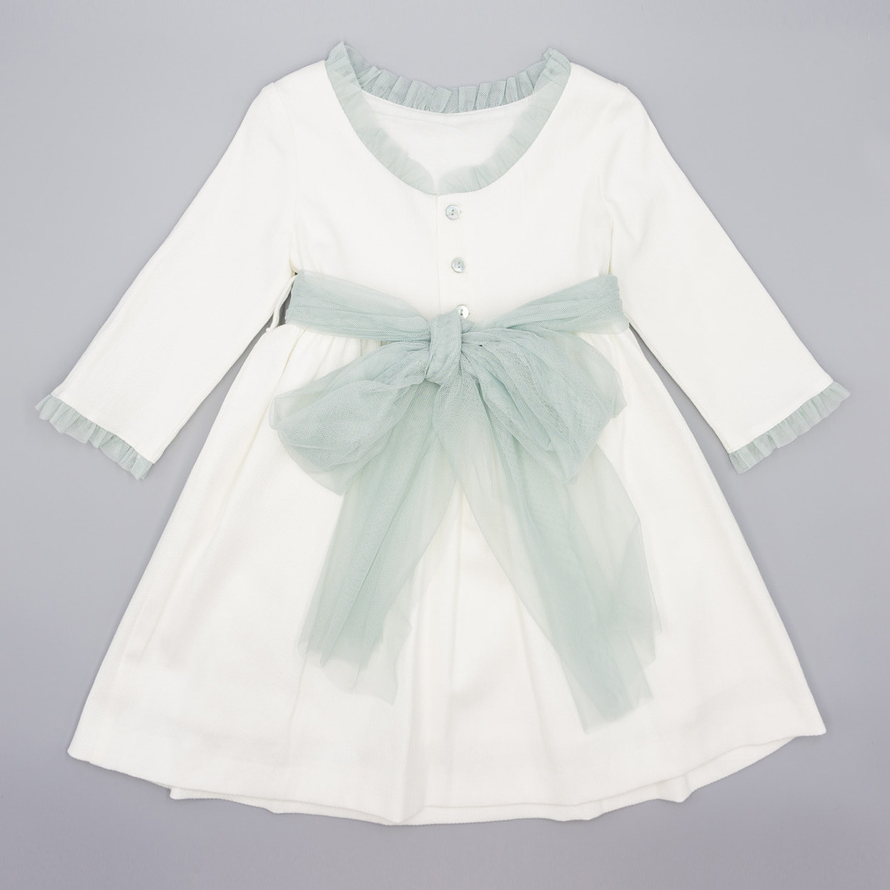 Vestido de pique blanco, con volantes en cuello y puños, y lazada en tul verde.