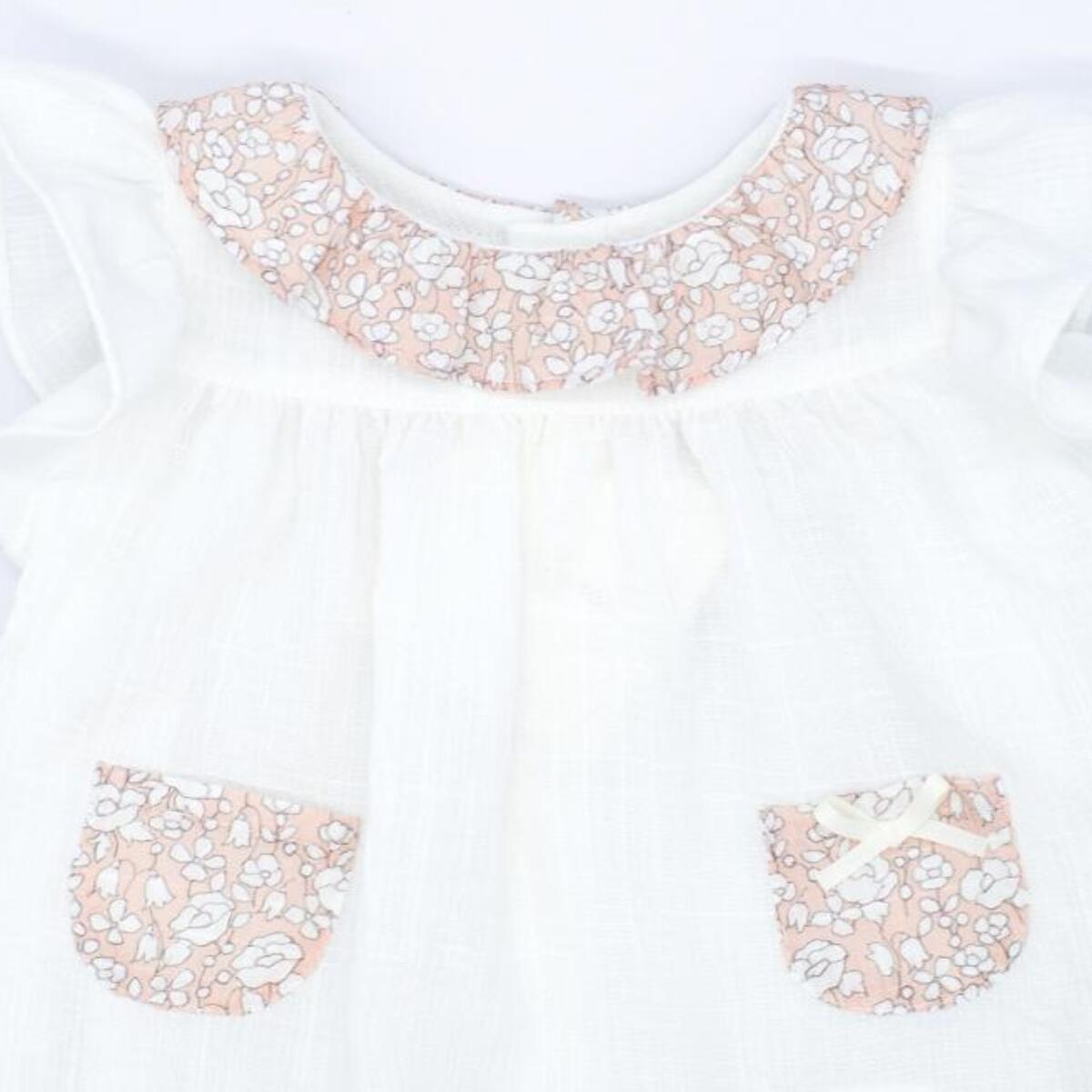 Blusa blanca con bolsillos y volante en el cuello de flores rosas, volantes en las sisas. Lazo en el bolsillo.