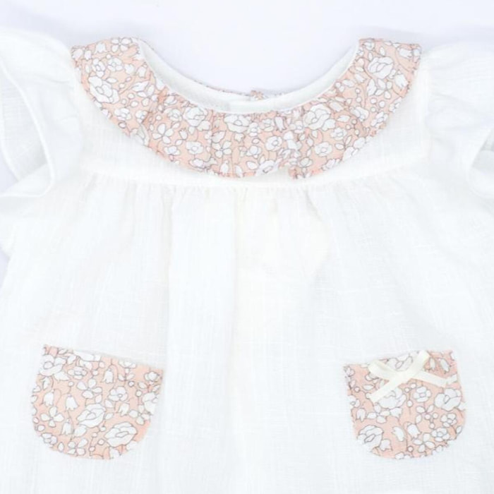 Blusa blanca con bolsillos y volante en el cuello de flores rosas, volantes en las sisas. Lazo en el bolsillo.