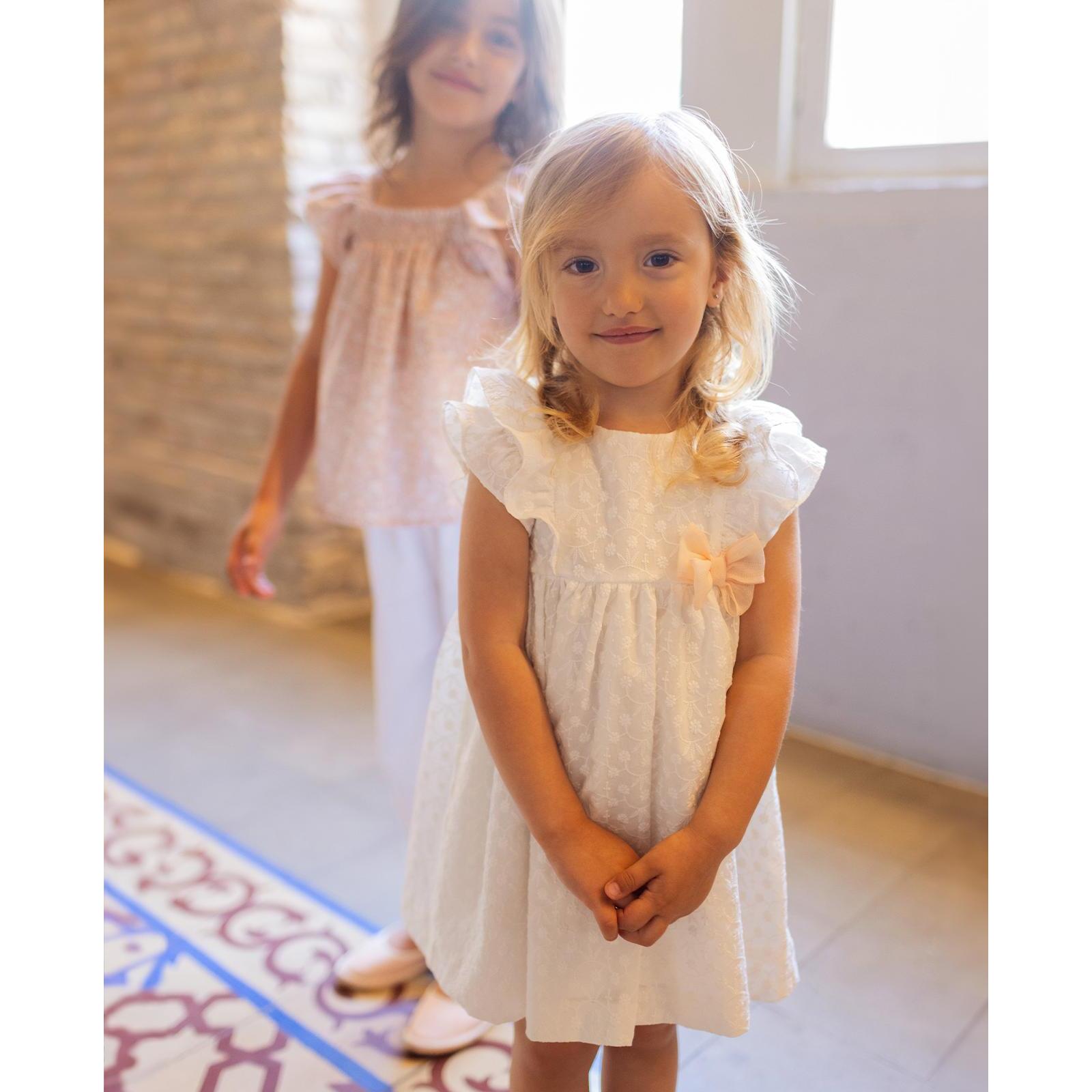 Vestido corto blanco bordado, volantes en la sisa y lazo rosa.